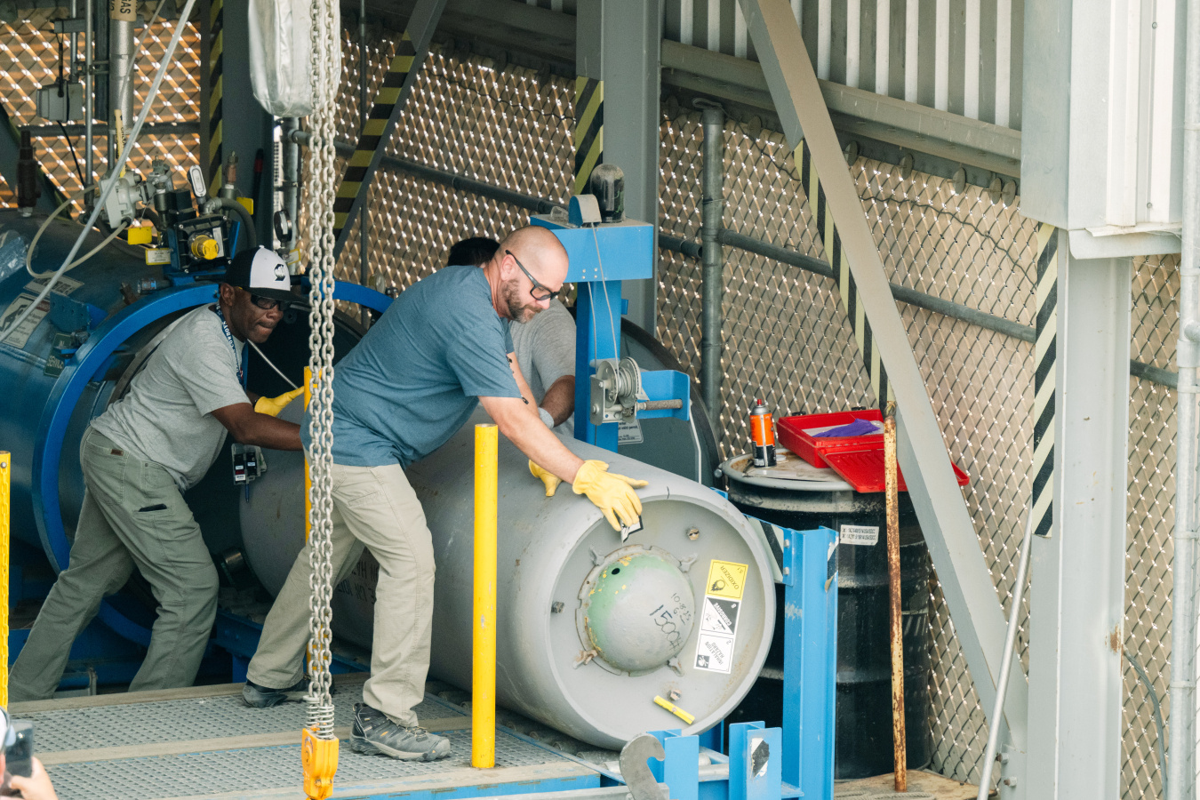 Employees moving a large grey canister inside a building
