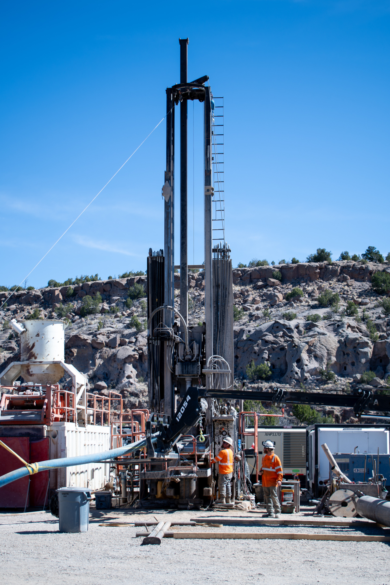 A large outdoor groundwater monitoring well at the Los Alamos site, two employees in protective gear stand beside it