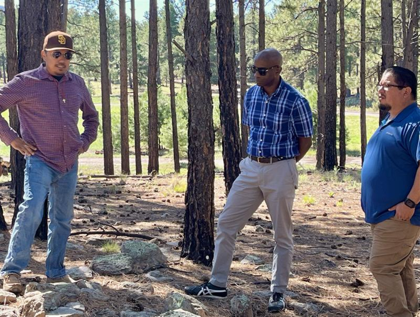 Three professionals standing in the woods at the Los Alamos site speaking to each other