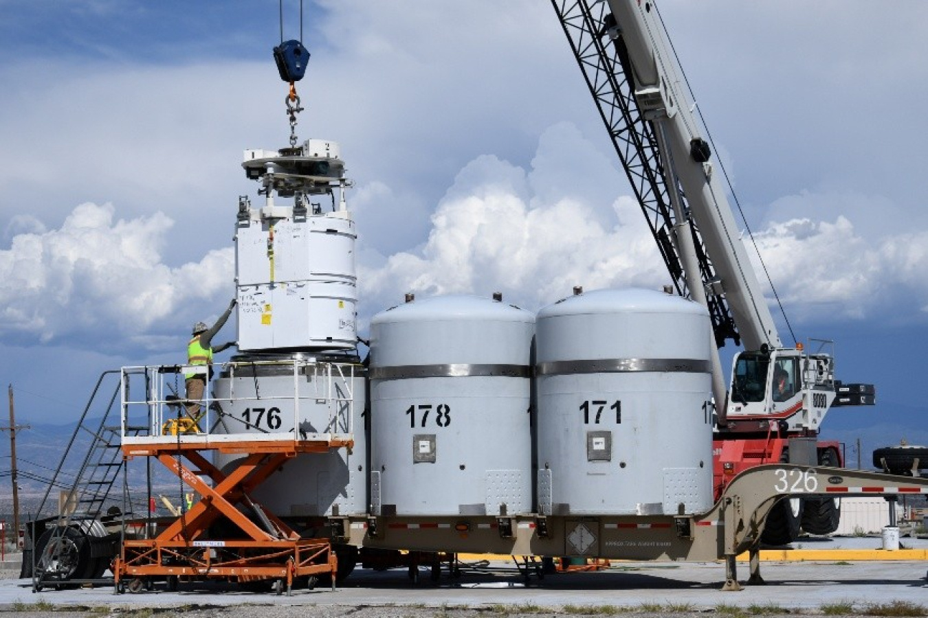 Crews loading large grey waste tanks onto a transportation cask