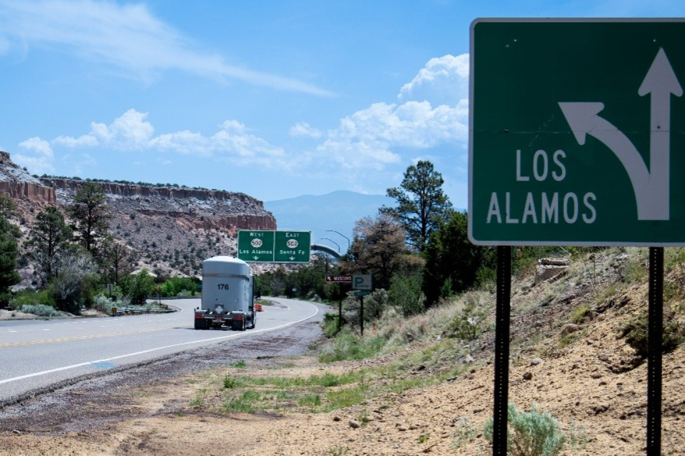 A truck with large white tanks on the back driving along a road beside a sign that says Los Alamos