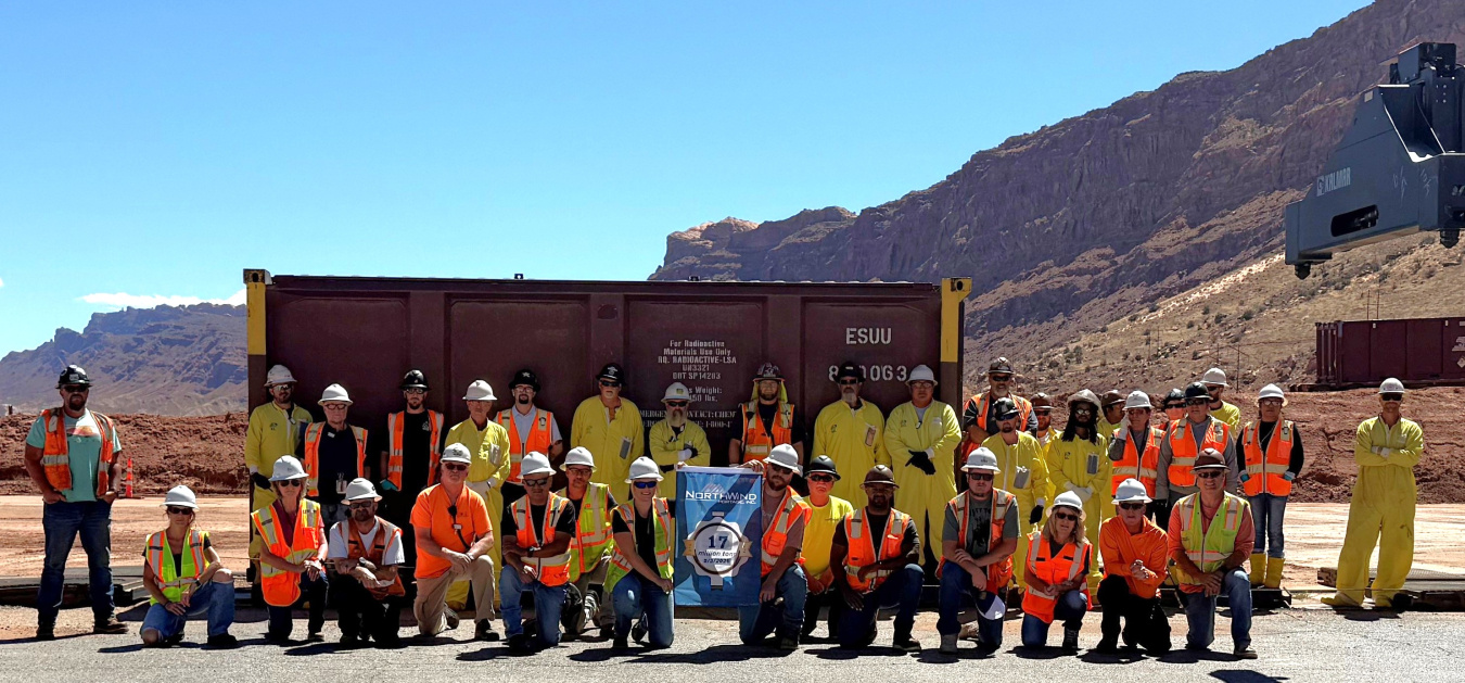 A large group of people wearing yellow and orange safety tear and white safety hats pose for a picture