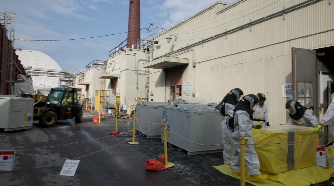 Employees in white hazmat suits working on large covered boxes at the Oak Ridge Site