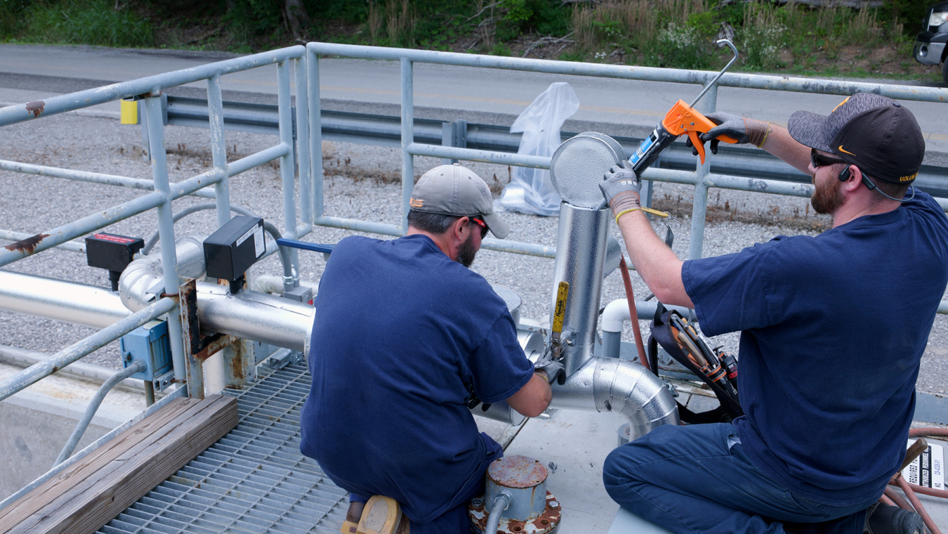 Two employees working with tool on metal piping at the Oak Ridge Site