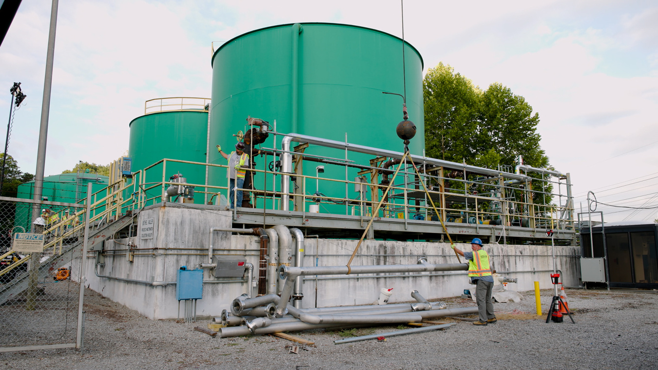 Multiple large green tanks with employees working on and around them