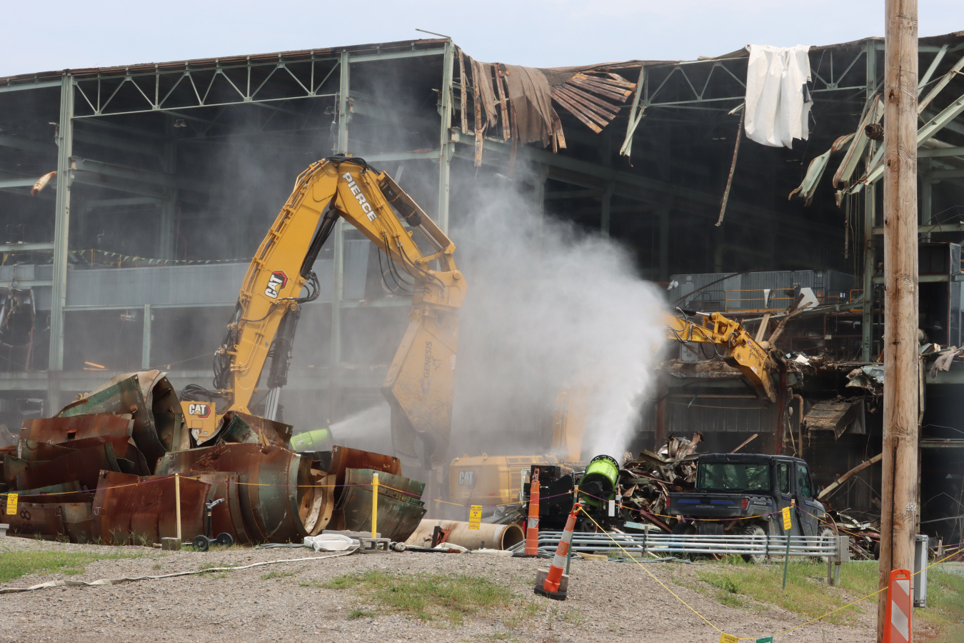 Construction vehicles carrying out demolition on a building with water being sprayed on it