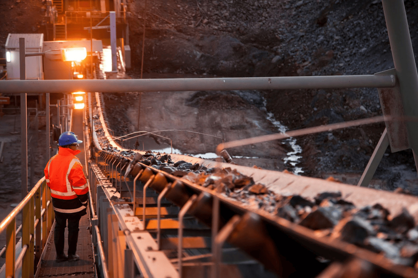Person in hard hat oversees mineral processing on conveyor belt