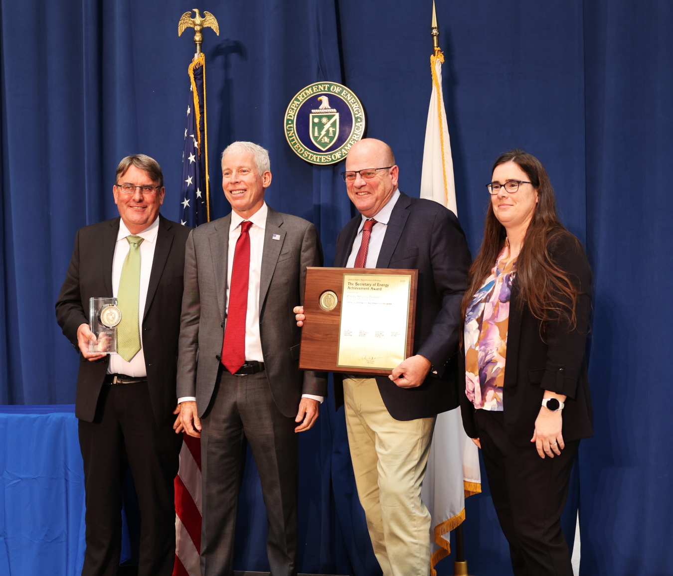 Four professionals pose for a photo with the Secretary of Energy, two people hold awards