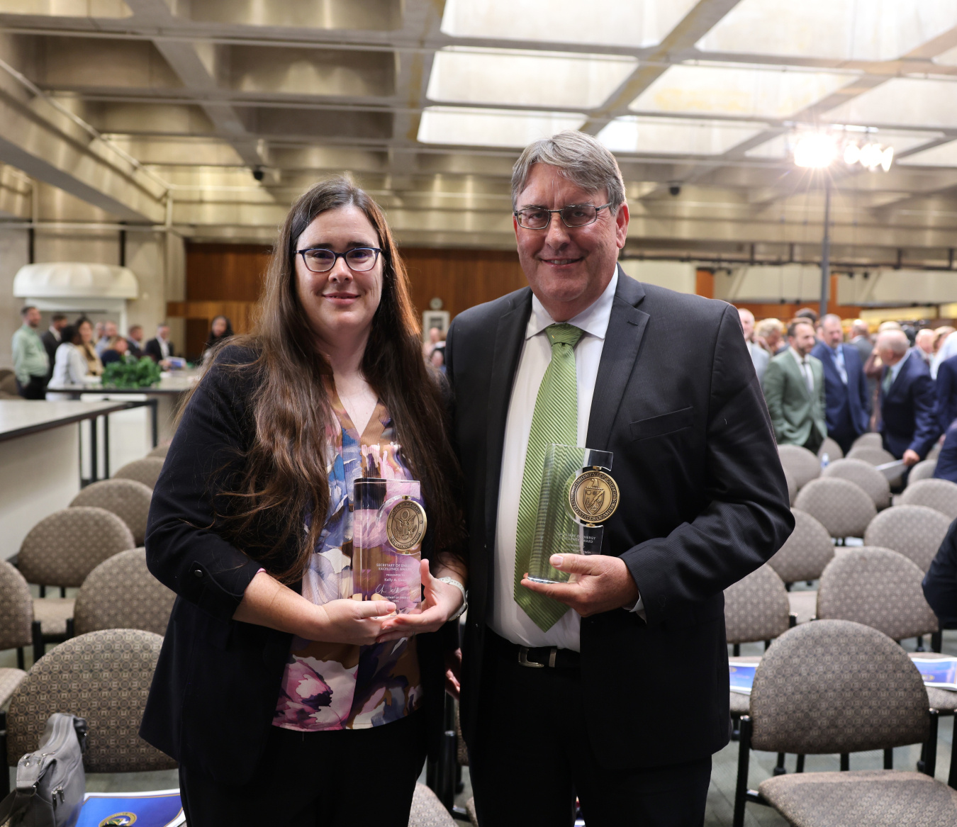 Two professionals pose for a photo together while holding awards