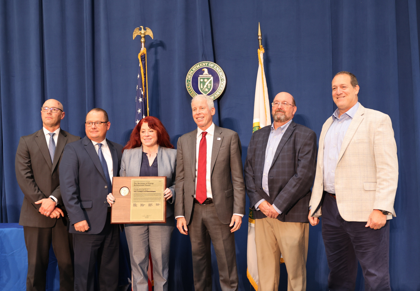 Six professionals pose for a photo with the Secretary of Energy, one person holds an award
