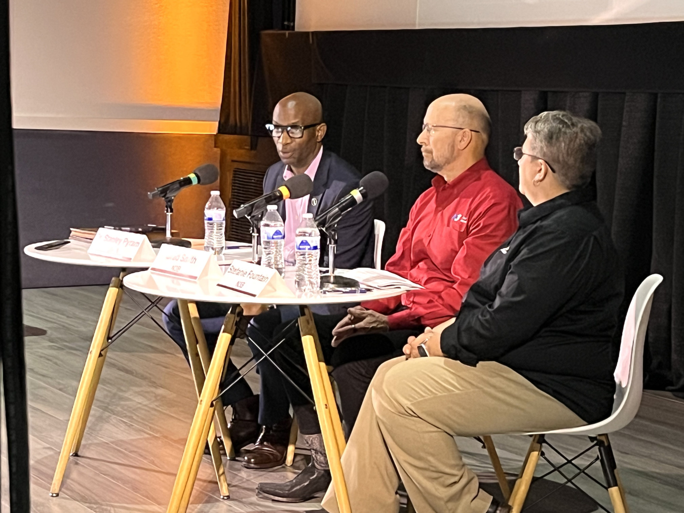 Three professionals sitting at a table speaking with each other and into microphones