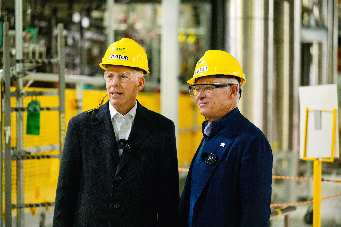 Two professionals standing in a laboratory building wearing yellow hard hats