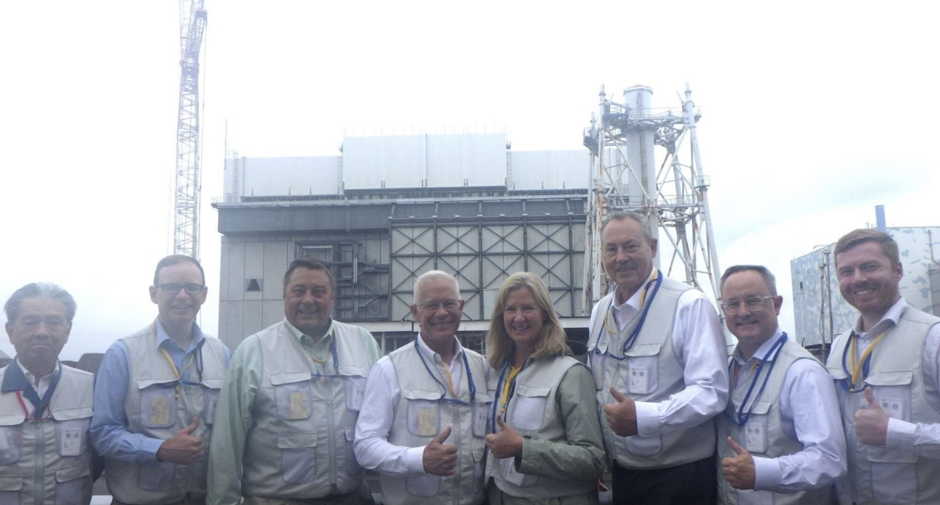 A group of EM leadership pose for a picture outside in front of a facility building while posing with a "thumbs up"