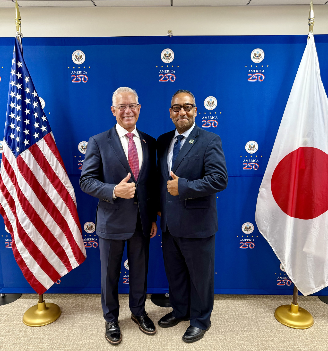 Two professionals pose for a photo together holding a "thumbs up