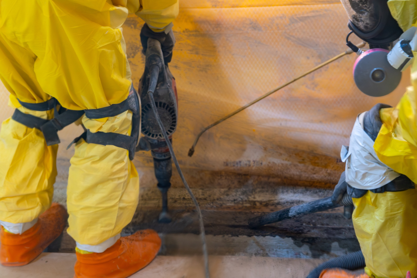 An up close shot of workers in yellow hazmat suits spraying liquid on a wall