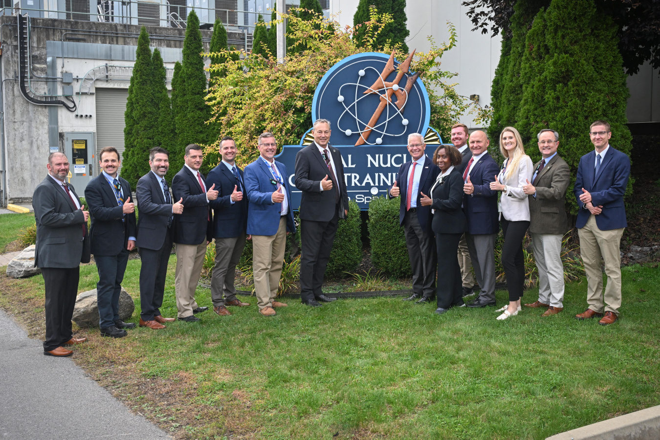 A group of DOE leadership posing for a photo by a sign with the nuclear symbol on it 
