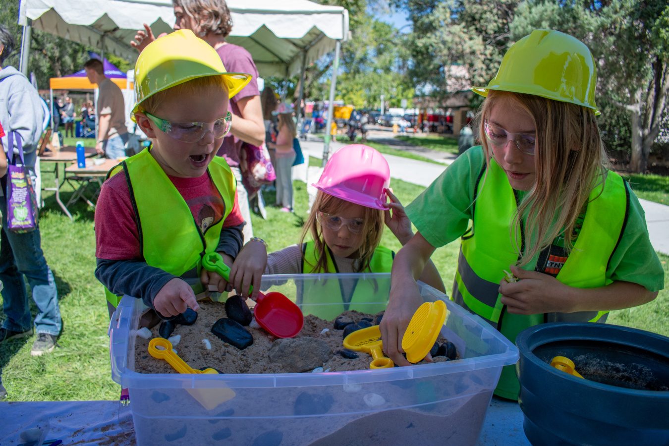 Children in yellow hard hats playing with toys in a sandbox