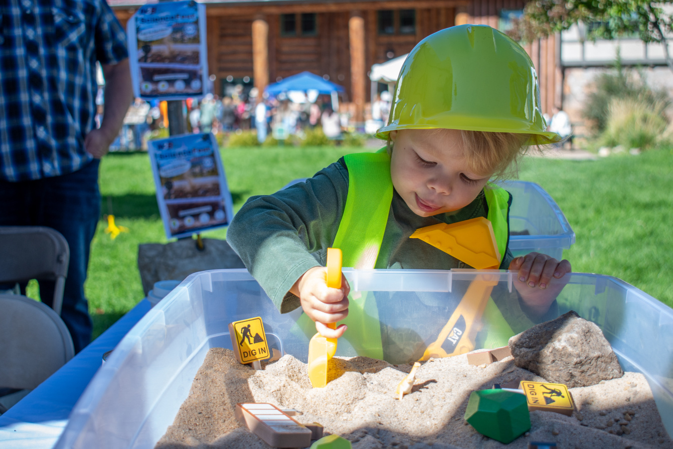 A small child in a yellow hard hat playing in a sandbox with toys