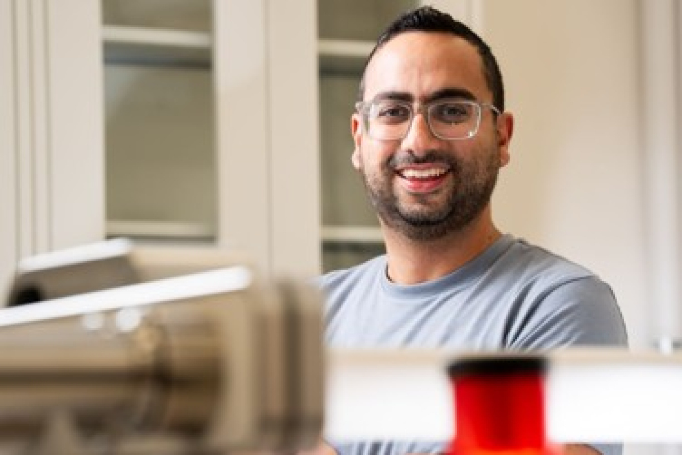 Elias Nakouzi smiles while standing in a laboratory behind scientific equipment.