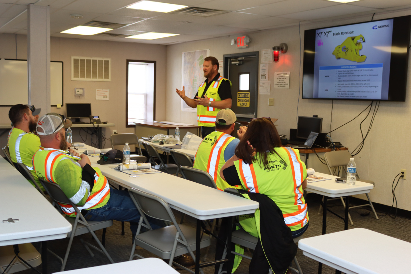 A group of professionals wearing safety vests sit in a classroom and participate in a training 