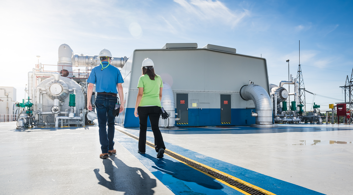 Two workers wearing hard hats walk past the steam turbine building at Robinson Nuclear Plant.