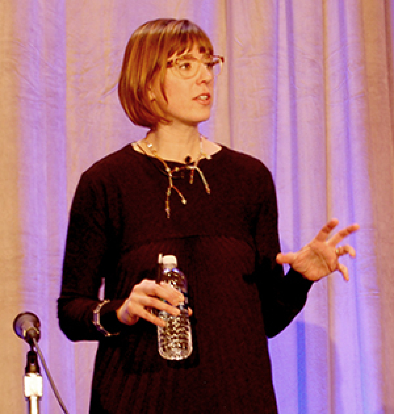 Woman standing at the front of a convention hall, addressing the audience.