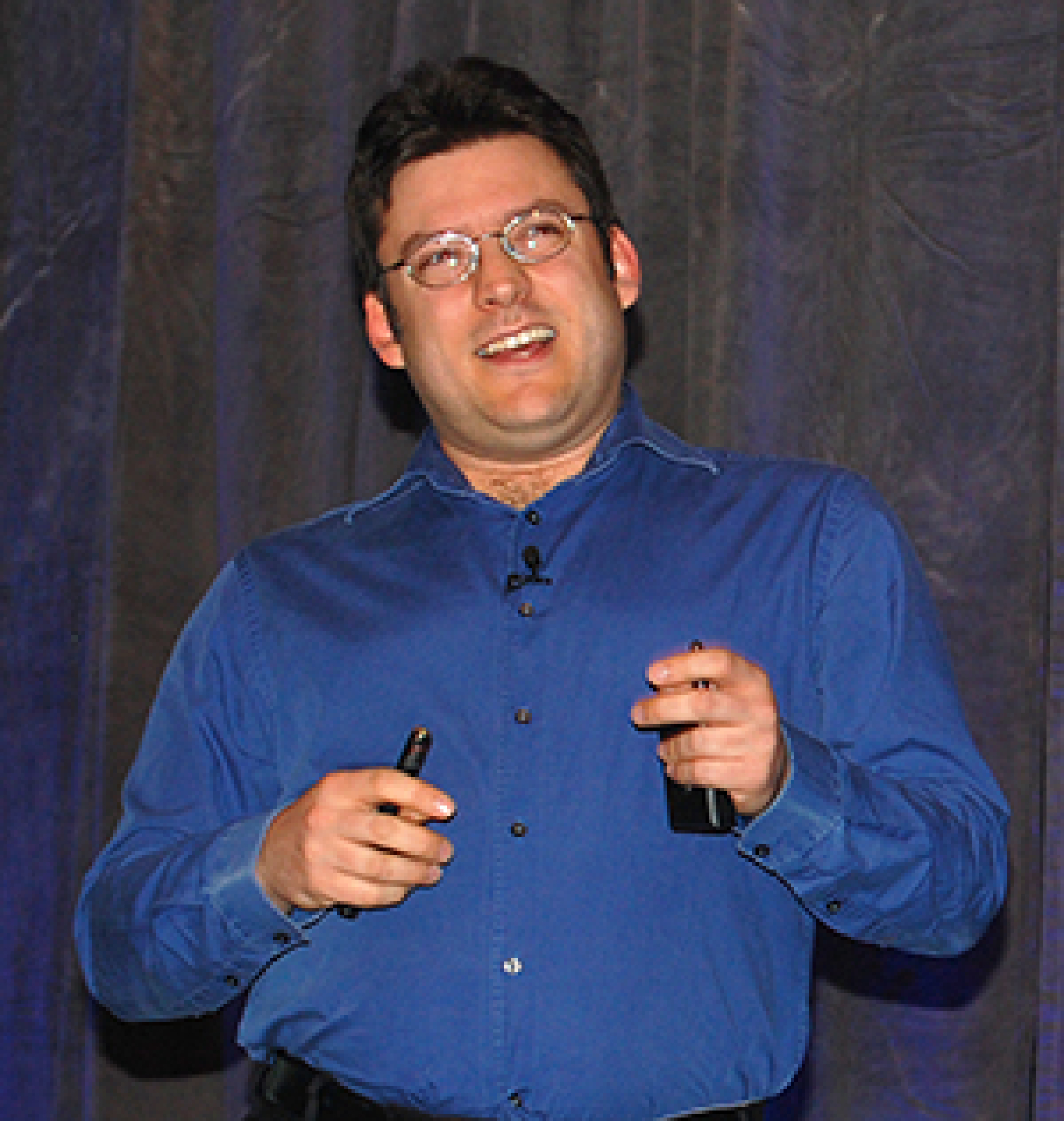 Man standing at the front of a convention hall, addressing the audience.