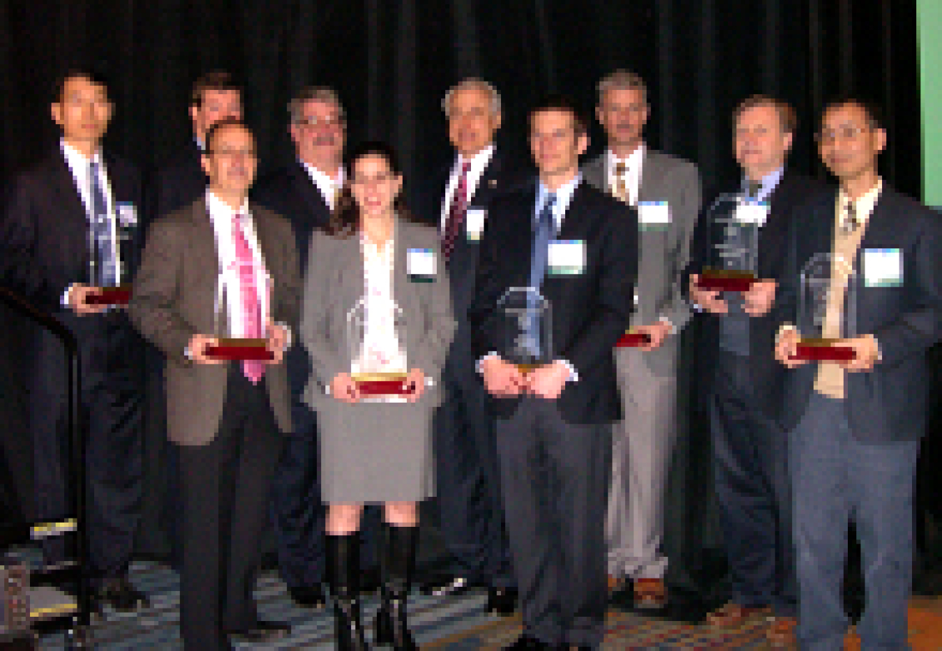 Photo of a group of people standing and facing the camera, holding award trophies.