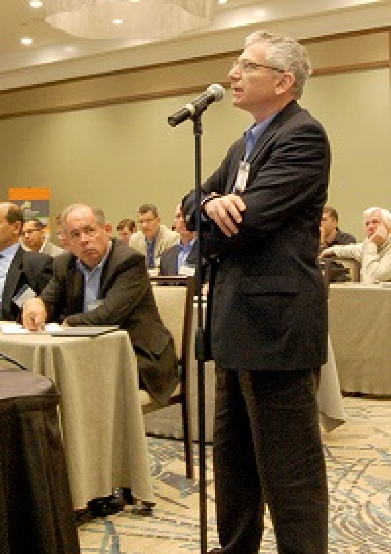 Photo of a conference attendee standing at a microphone in the audience, asking a question.