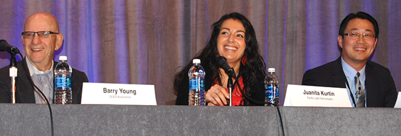 Three people sitting at a table as panelists in front of the audience.