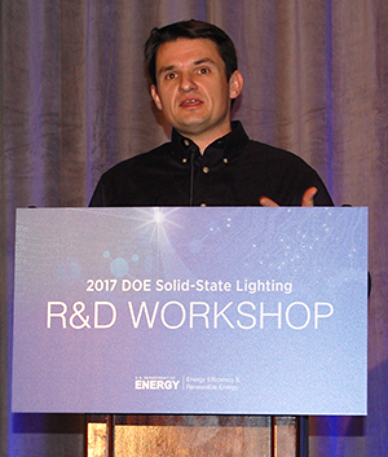 Man standing at the front of a convention hall, addressing the audience.