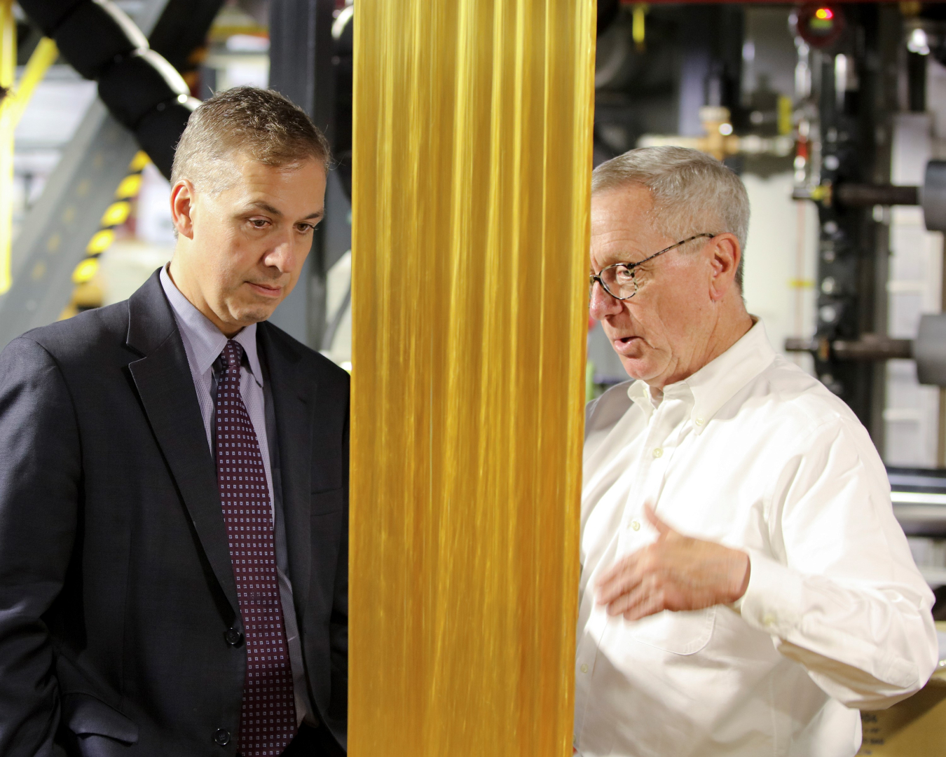 Photo of Michael Berube, left, listening to an Oak Ridge lab researcher, right, who is explaining a piece of partially oxidized material being converted into carbon fiber at the lab.