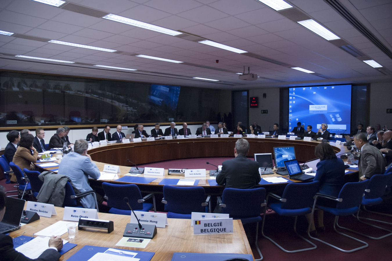 Photo of a large meeting room with people seated around a circular table.