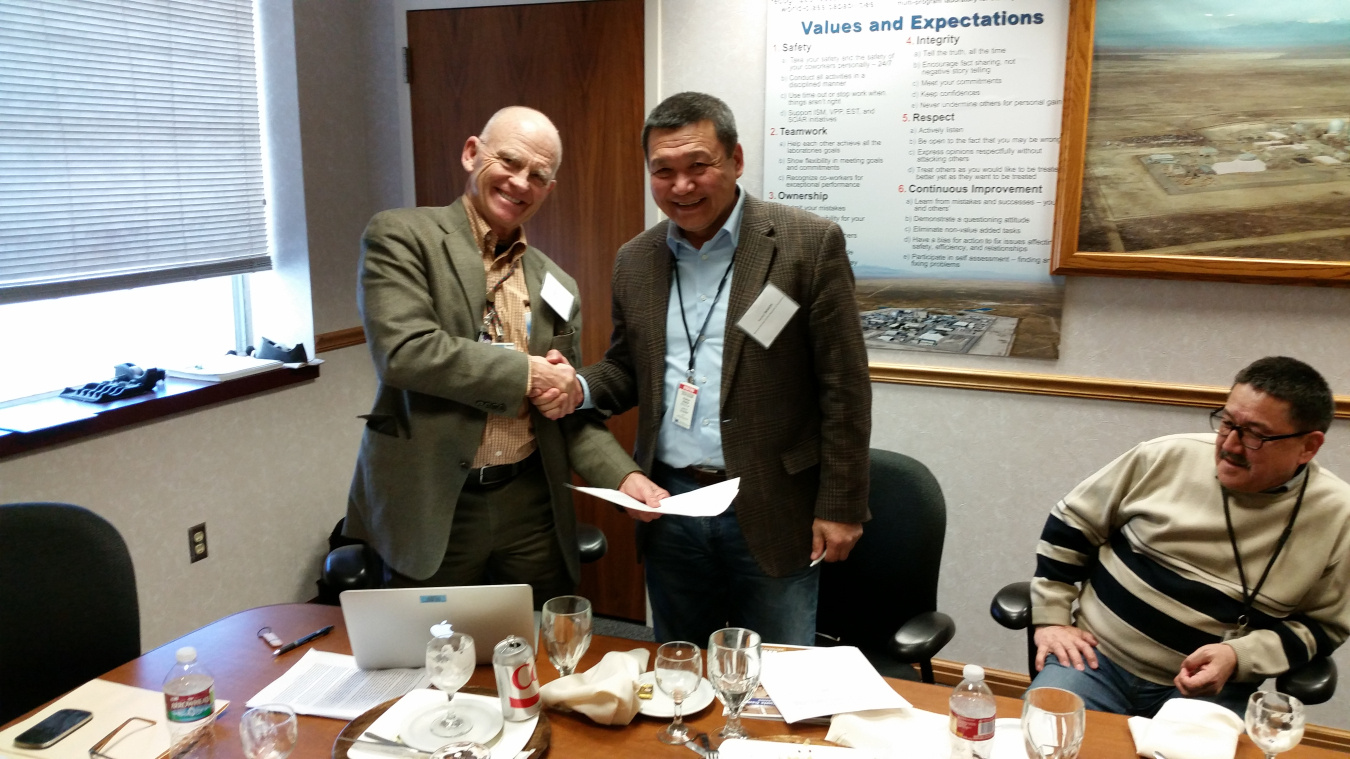 Two men standing and shaking hands, looking at the camera.