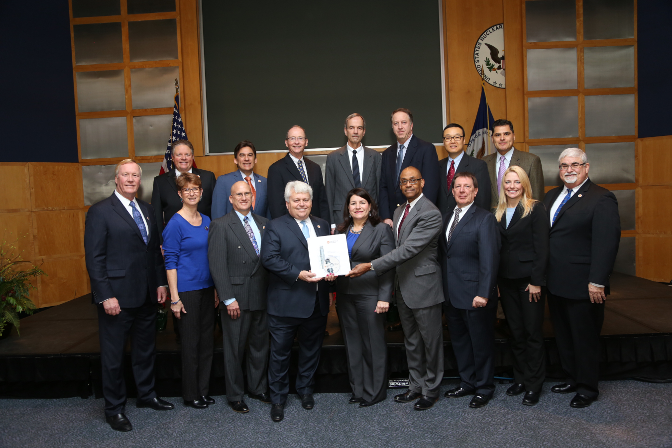 Group photo of men and women in business attire facing the camera, standing at the front of a room. See the caption below the photo for identifications.