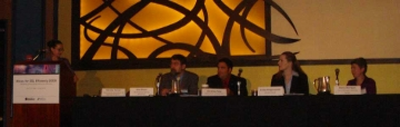 A photo of a panel of four speakers sitting and a moderator at the podium.