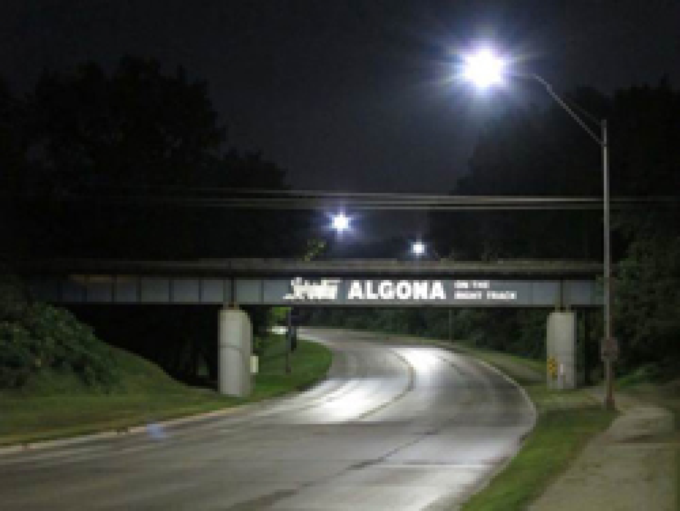 A road at night winding under an overpass, with light posts nearby.