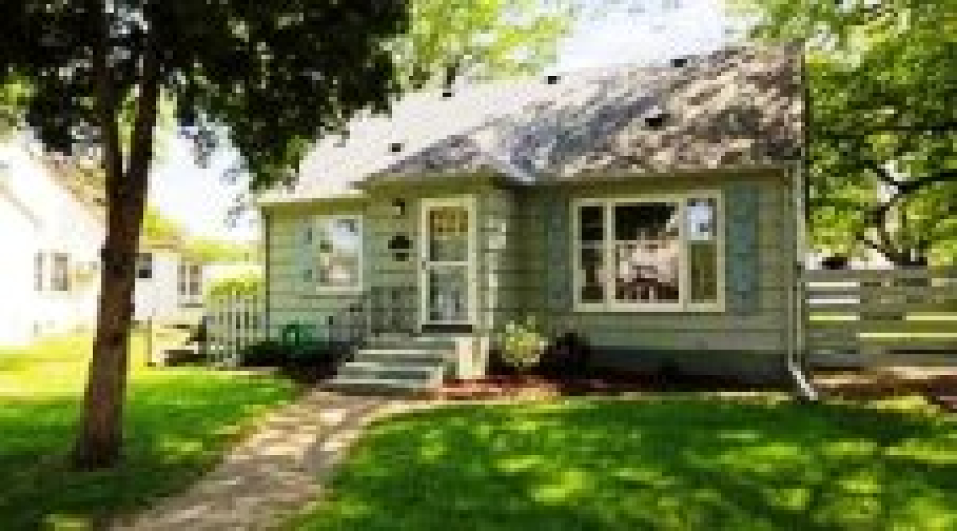 Photo of a small house from the front, with a tree shading the house and expanse of front lawn.