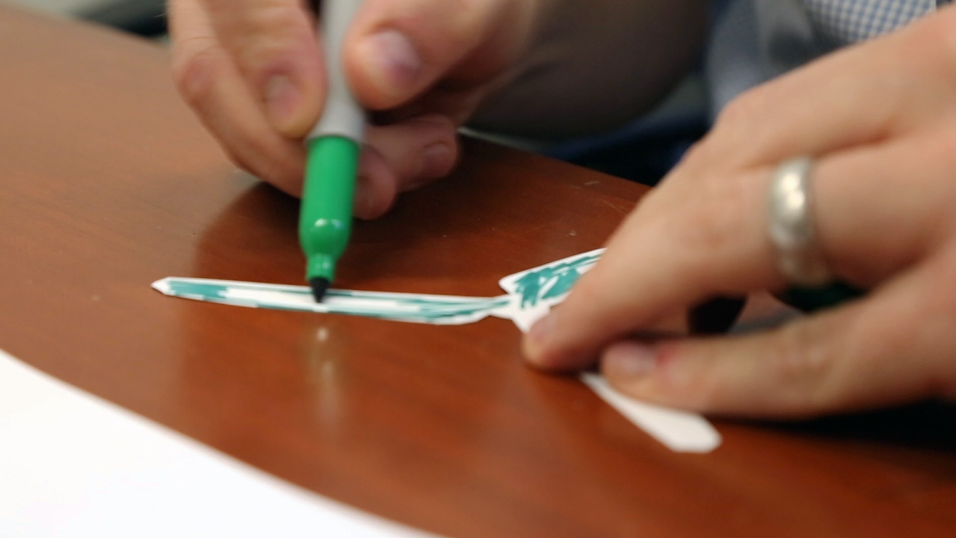 Two hands coloring a strip of paper with a marker. 