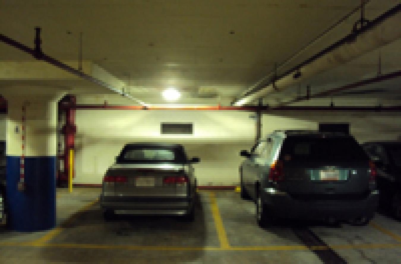 Photo of cars in a parking garage with an LED fixture on the ceiling above.