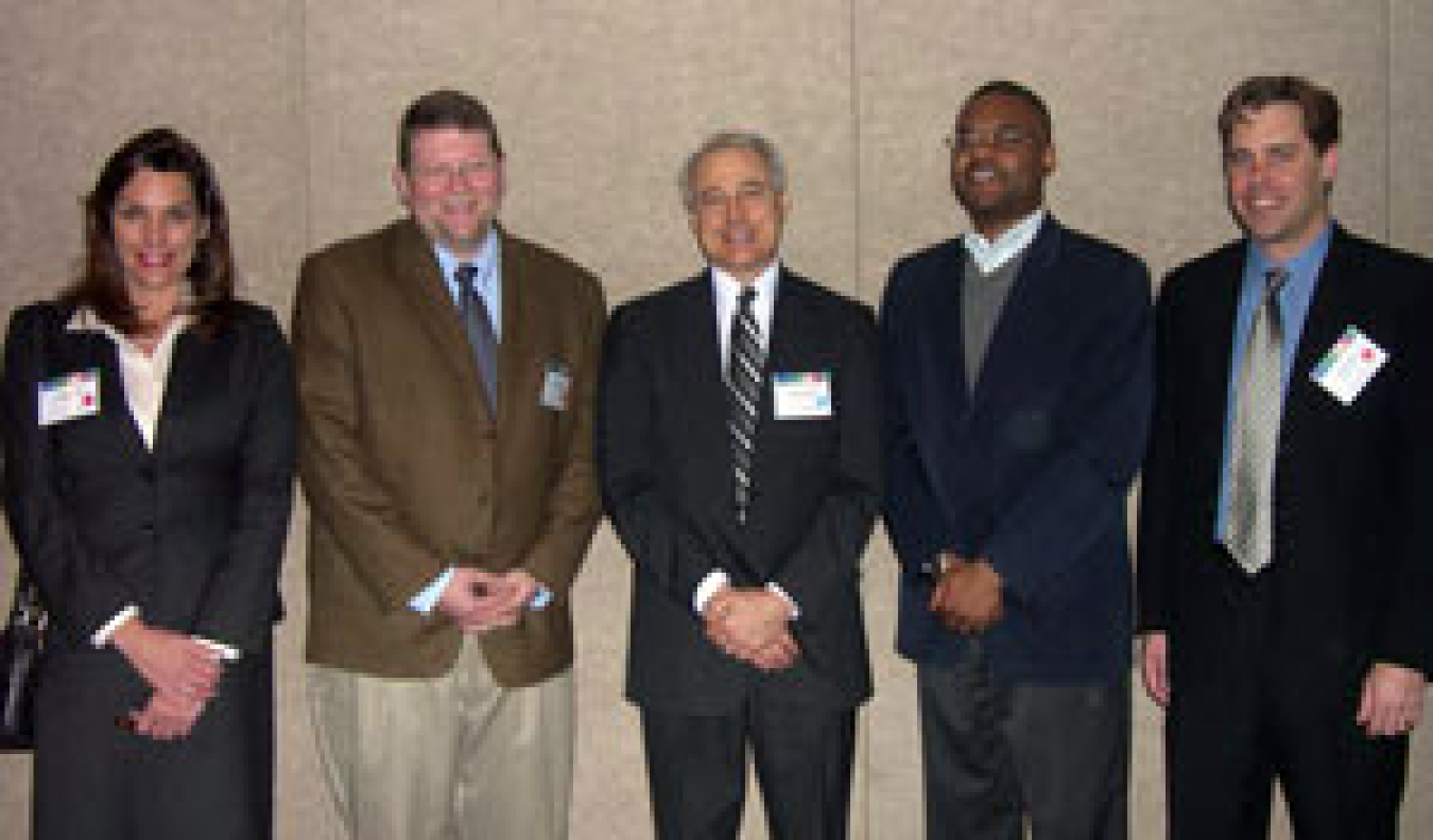 Photo of a woman and four men, standing, smiling at the camera.