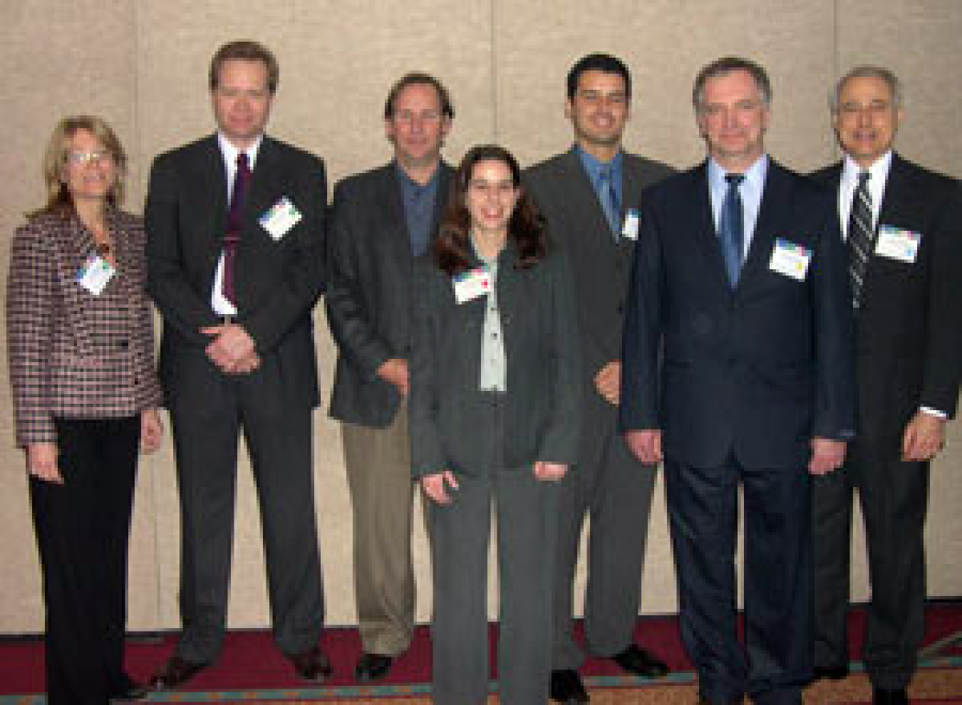 Photo of a man and woman in front, and a woman and four men in back, standing, smiling at the camera.