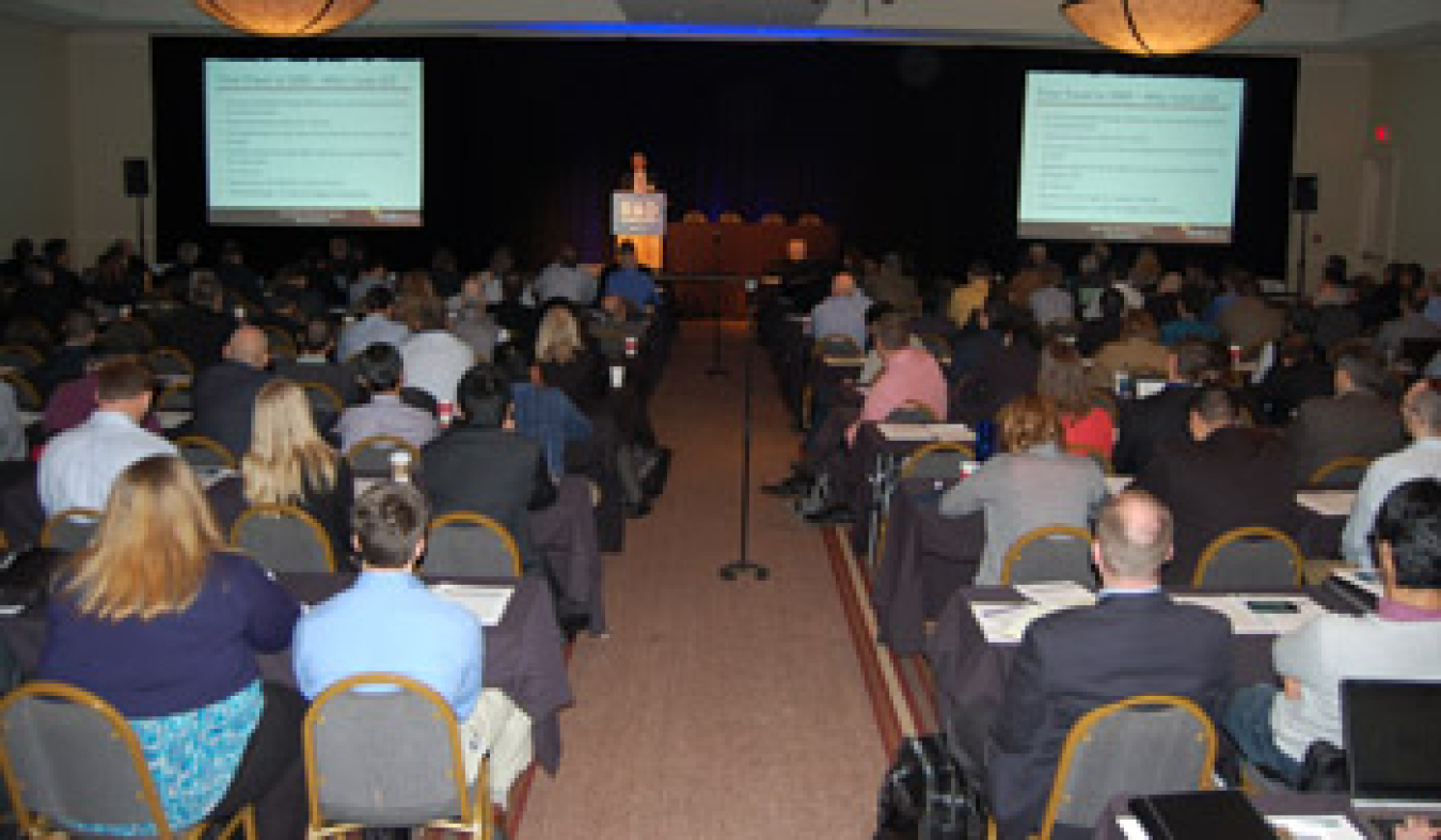 A view from the back of the room of a group of people seated, listening to a speaker.