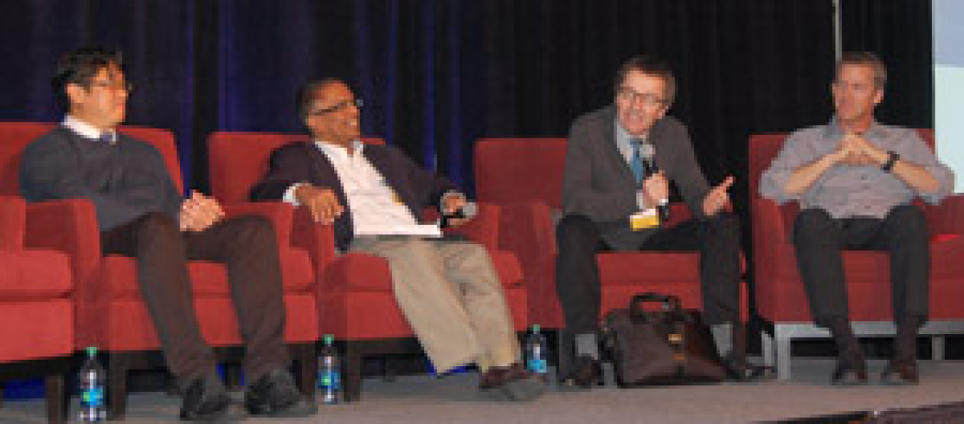 Four men seated in individual chairs at the front of the meeting room.