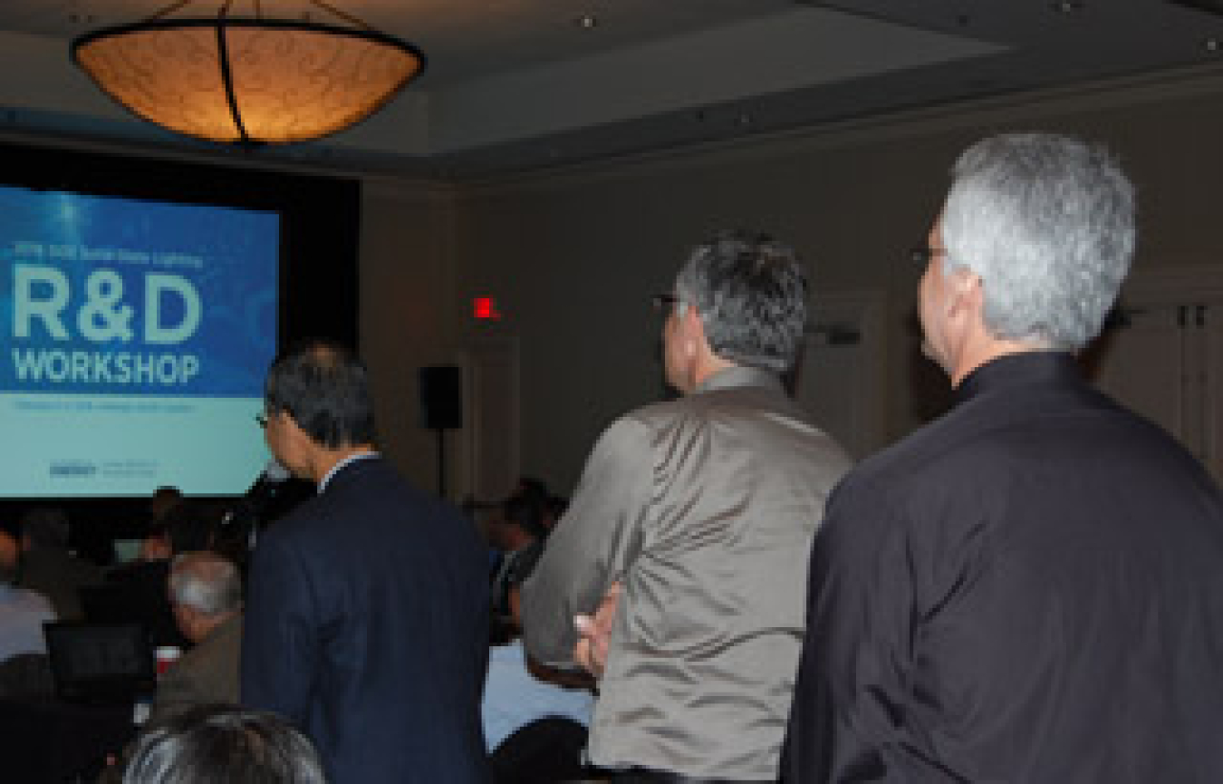 The backs of a few men standing and facing toward a presentation screen in a meeting room.