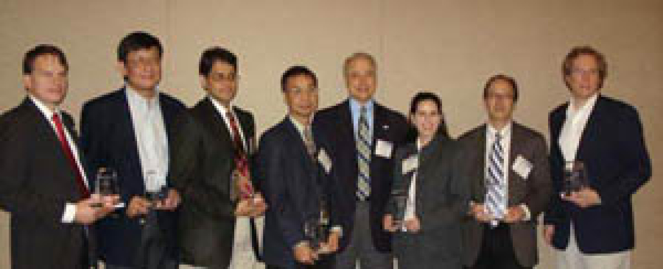 Photo of eight people standing in a line, seven of them holding awards.