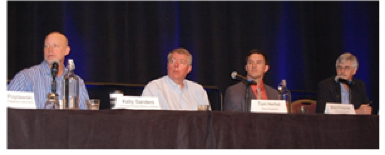 Four people sitting at a table with microphones, addressing an audience during a session.