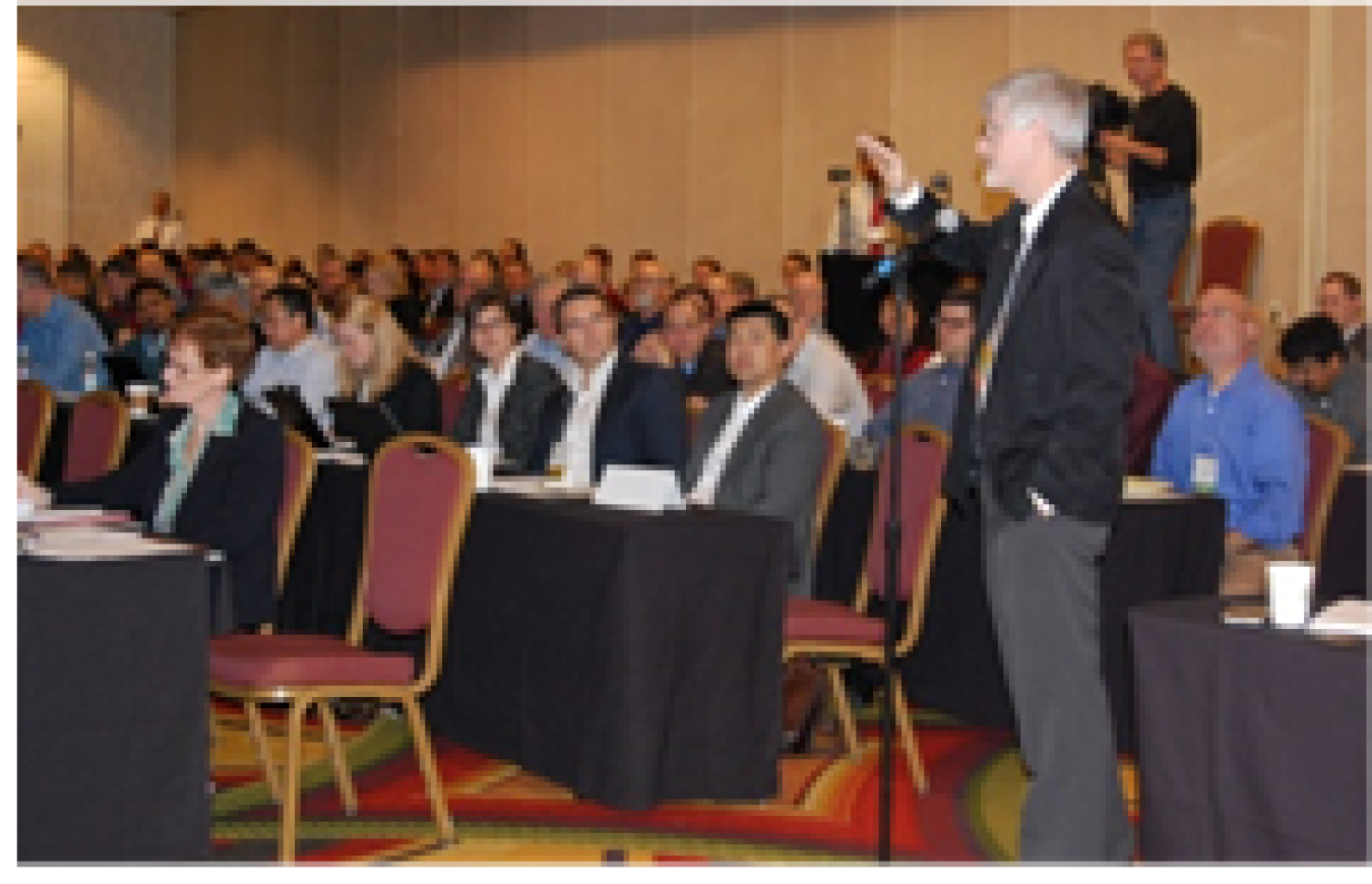 Group of people sitting in chairs in an audience, in a large meeting room.