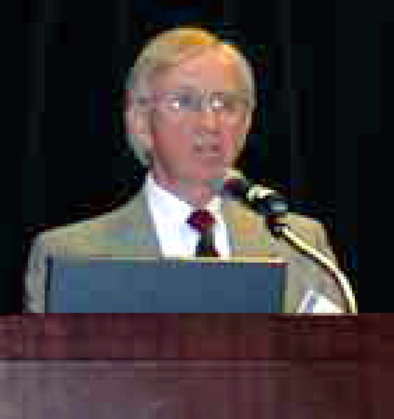 Photo of a man in a suit speaking at a podium.