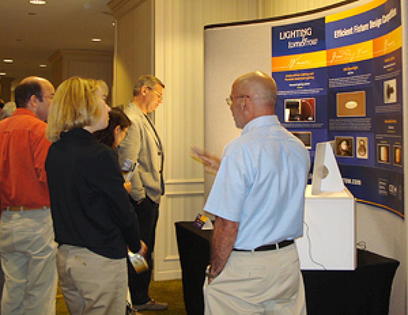 Photo of several people standing in front of and looking at a lighting exhibit, with one man explaining something to the woman beside him.